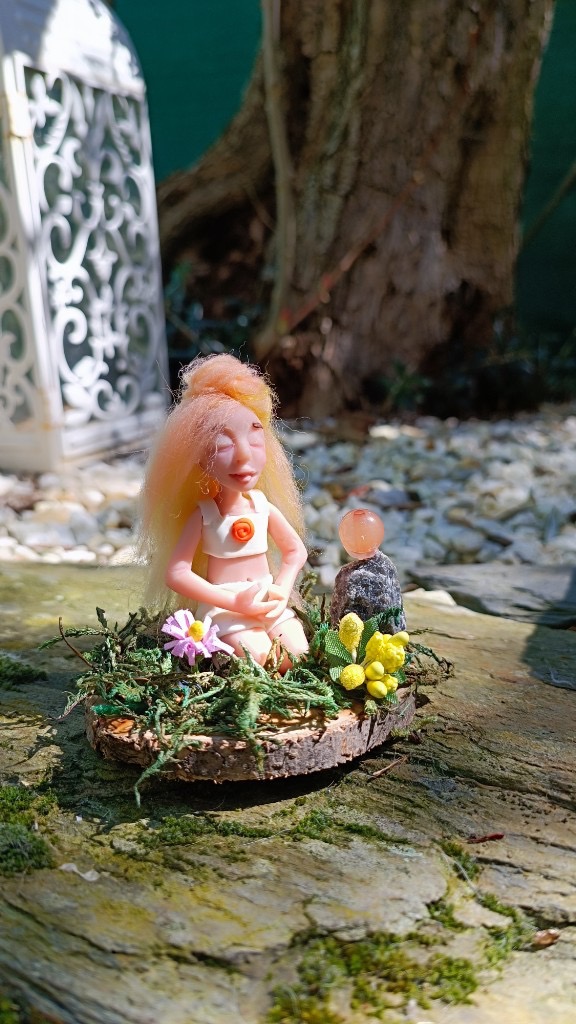 Figura meditando con pelo melocotón, flores amarillas y esfera naranja en la base