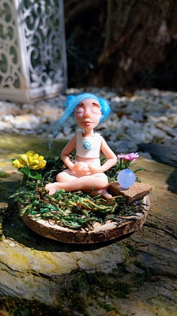 Figura en loto con pelo azul afelpado, top blanco y flores en musgo