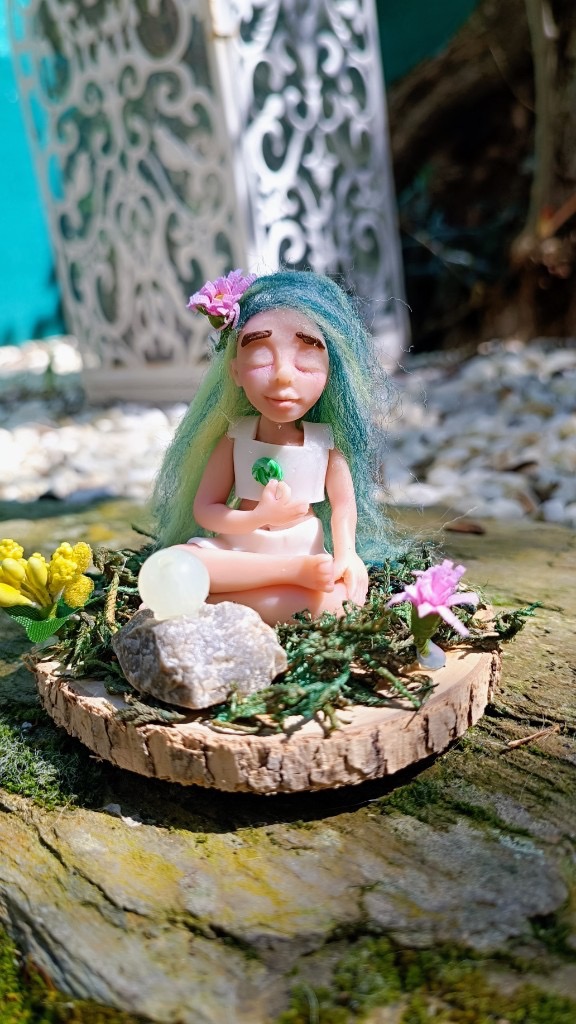 Figura meditando con pelo verde-azul, mano al pecho y orbe blanco en la roca