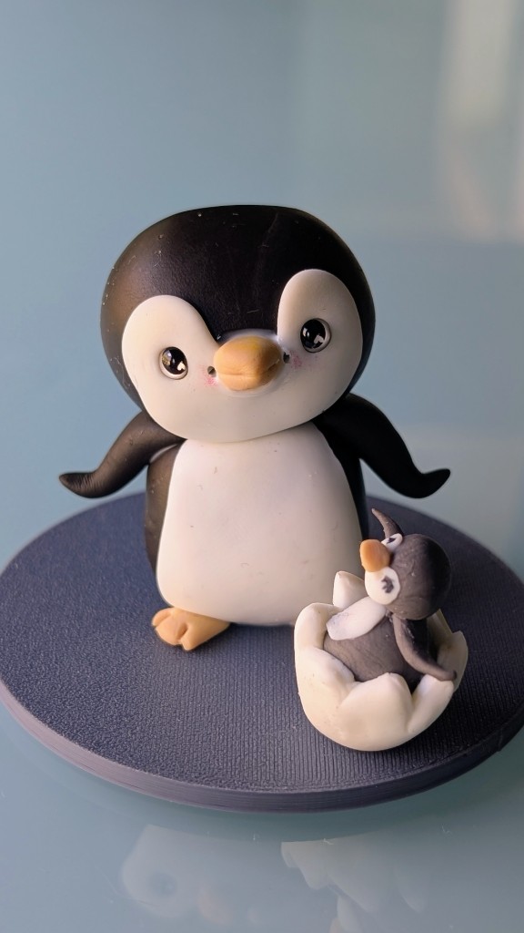 Figura de pingüino adulto con cría saliendo del huevo, modelada en porcelana fría
