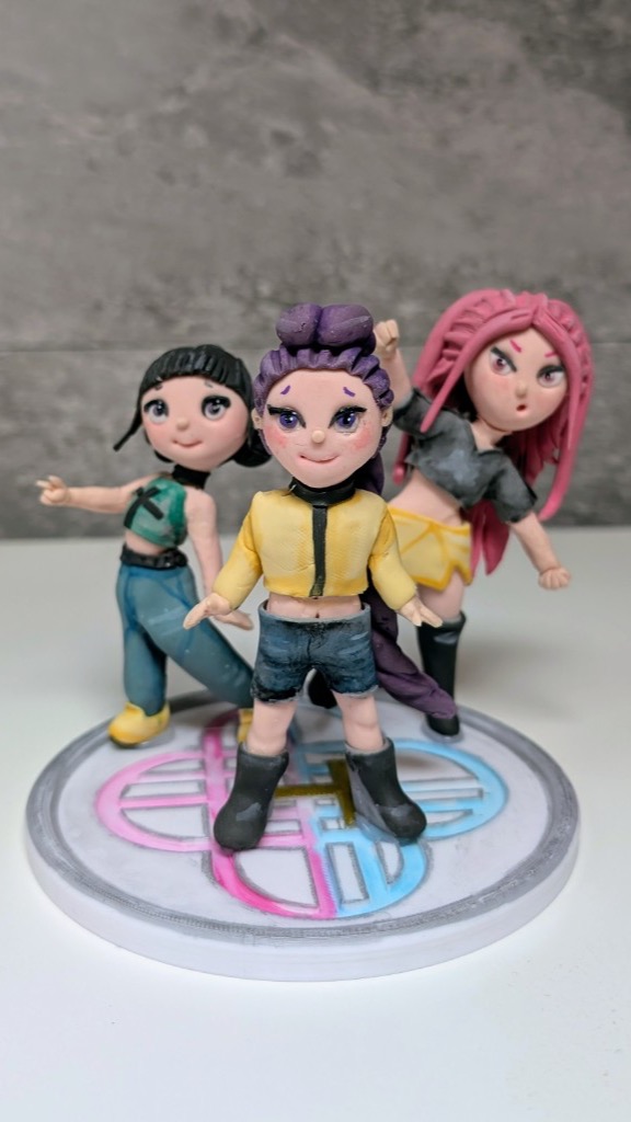 Tres figuras chibi de guerreras K-pop Demon Hunter con pelo de colores sobre base decorada en porcelana fría