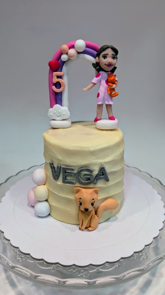 Tarta infantil con niña, gato, arcoíris y letras decorativas en porcelana fría
